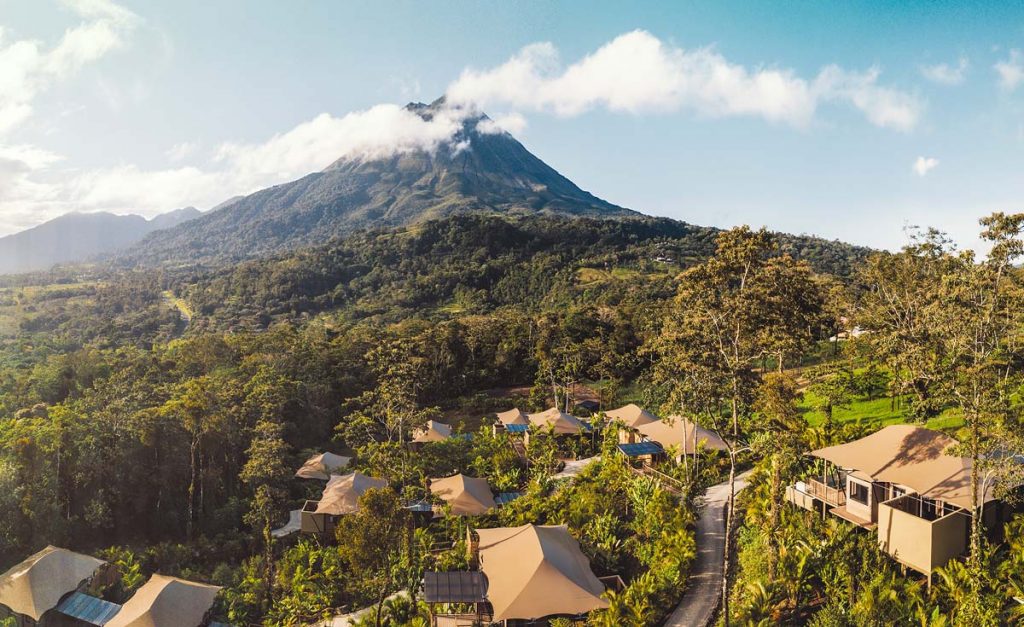 Small houses with brown roof within the rainforest and a volcano is in the background