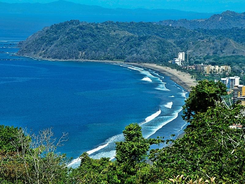 Beach with blue sea from above with mountains and rainforest and houses