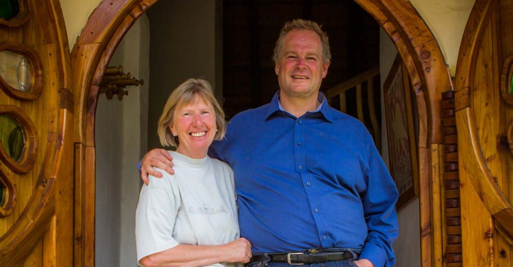 A woman and a man are standing in a doorway and smiling. The man is placing its hand on the woman's shoulder. 