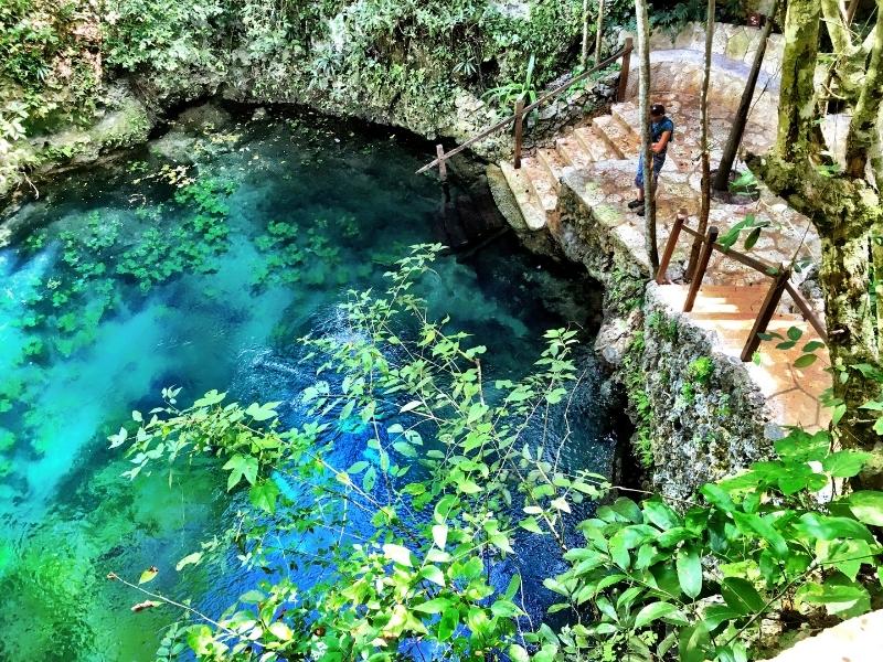 Green-blue cenote with steps to get in surrounded by green fauna.