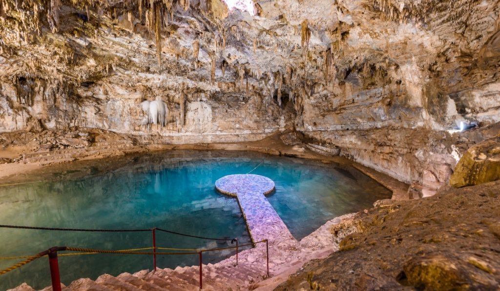 A round platform in the middle of a turquoise blue lake inside a large cave.
