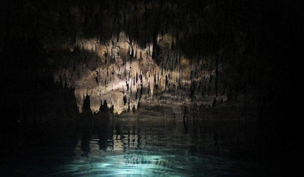 Dark cave with a really small light source where you can see light blue water