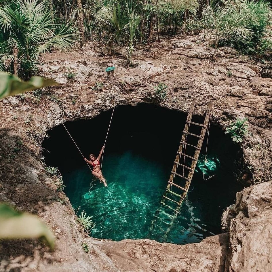 Sinkhole with ladder and woman swinging in the water.
