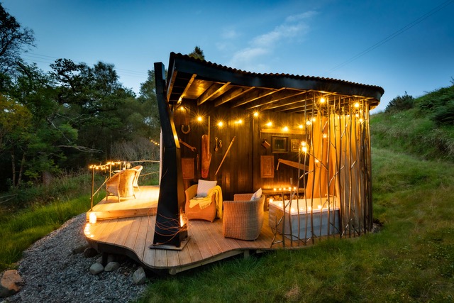 Small wooden hut with twinkle lights and a wooden deck with a bath tub