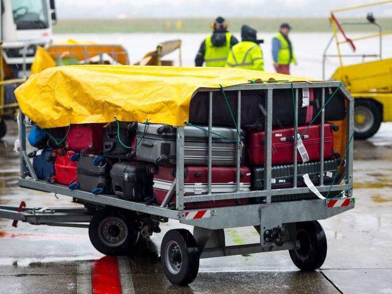 An airport cart full of luggage covered with a yellow tarp