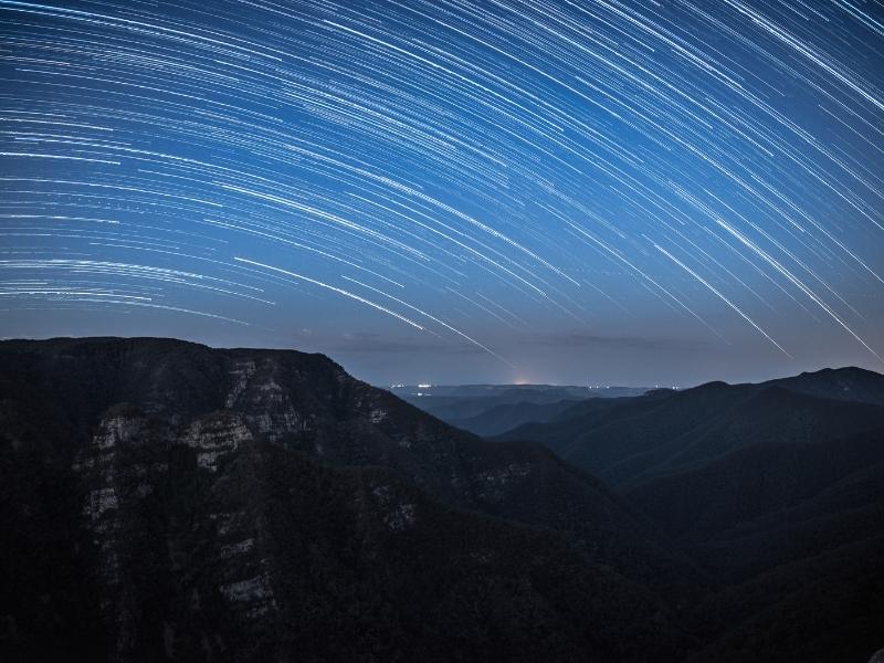 The movement of the stars draw lines on the night sky above the mountains