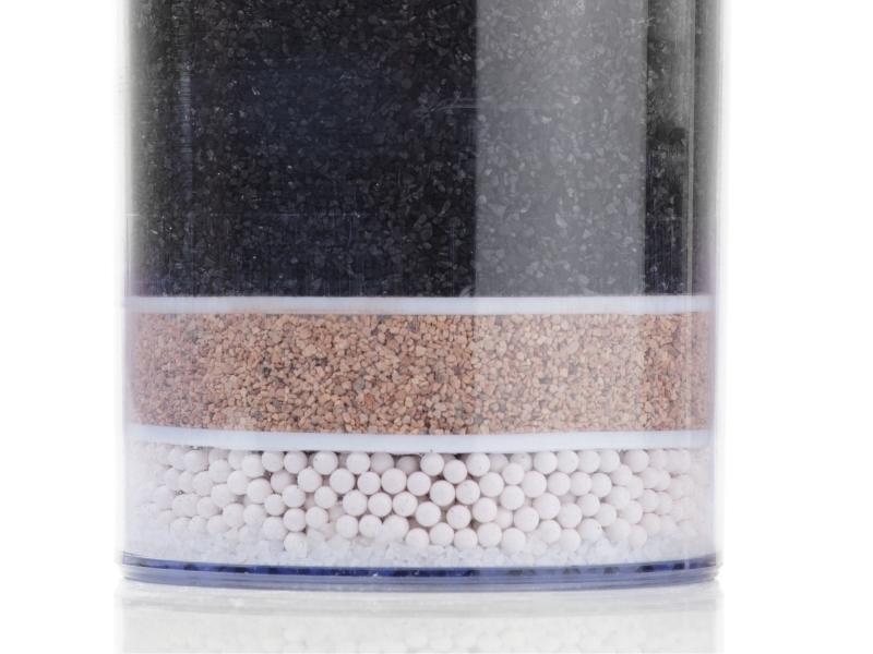 A tall glass container with layers of small white pearls, then gravel, then active charcoal