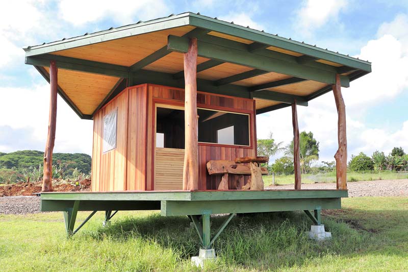 Small wooden hut on stilts painted green and natural brown with a small window and door.