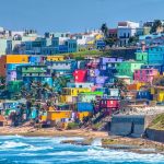 Small houses in the color of the rainbow spread along a hillside next to the ocean