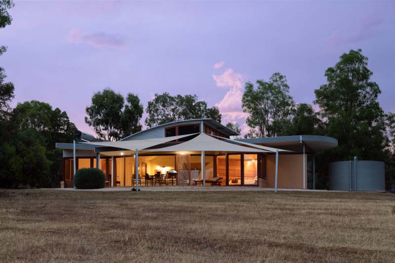 A one-storey building with huge glass windows and doors and a front terrace covered with white canvas. 