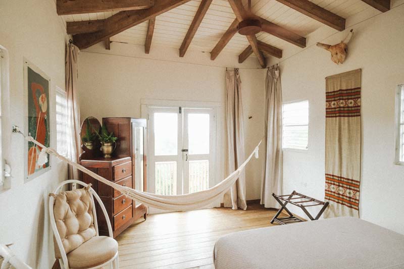 A room with white walls and doors. There is a bed, wardrobe, chair and a hammock