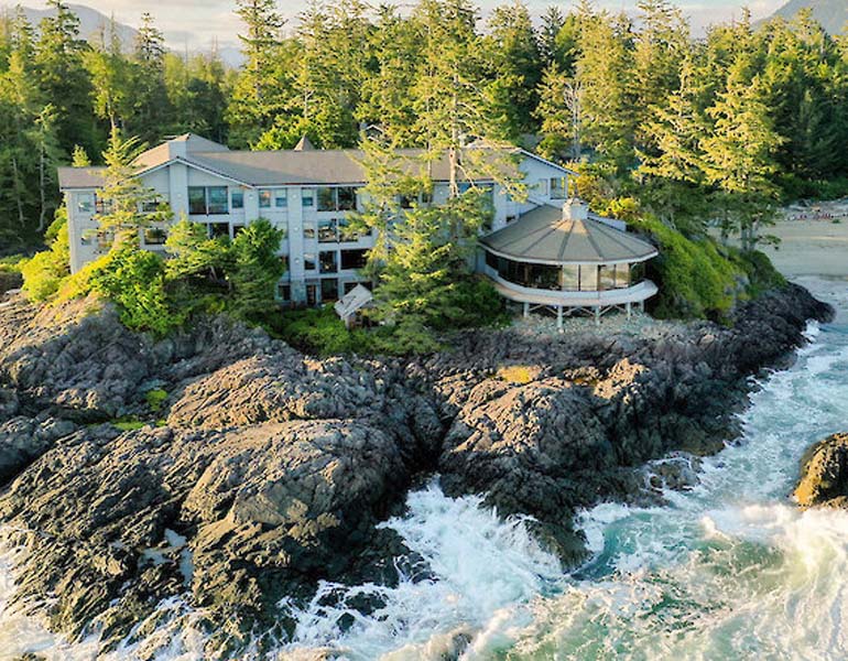 A 3-storey building that was erected right on the cliffs next to the ocean. The waves are crashing to the cliffs. 