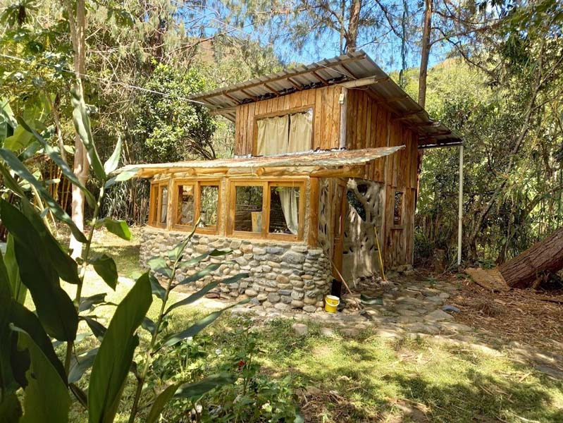 A small cottage in the middle of the rainforest built with round stones, wooden and metal roof. 