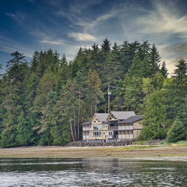 A yellow wooden two-storey house on the seaside surrounded by forest. 