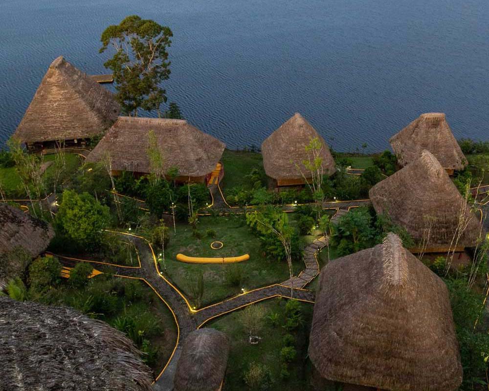 Several cottages with thatched roof pictured from above is situated near a lake with small paths connecting them