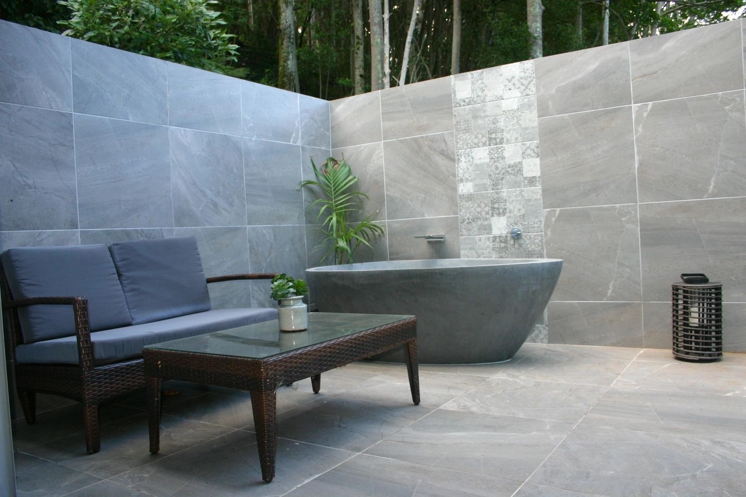 Open air bathroom with grey tiles, grey bathtub and lounge chair and table