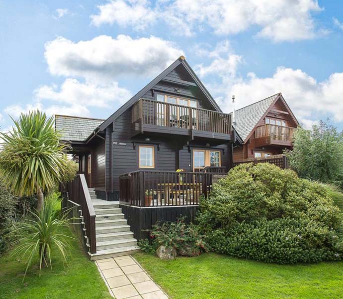 2 dark wooden two-storey houses with balcony and front porch and a lush green garden in the front