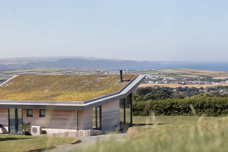 A wooden house with grass roof is on top of a hill looking over a small town far away. 