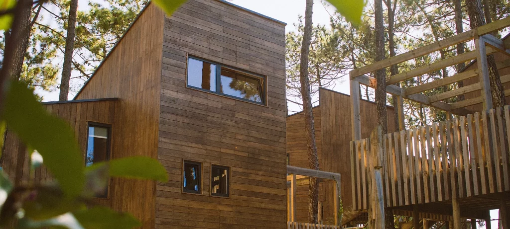 2 storey building with small windows completely covered with wood panels. It is surrounded by trees. 