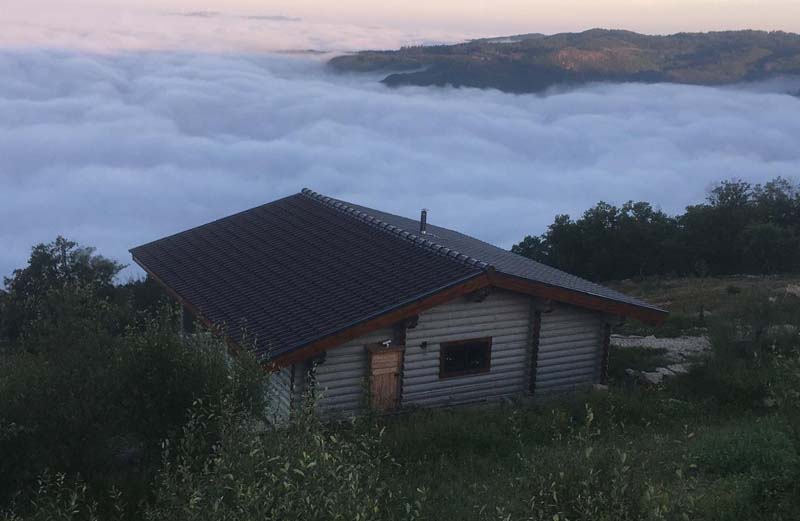 Small wooden hut on top of a hill overlooking a valley which is now covered with thick clouds. 