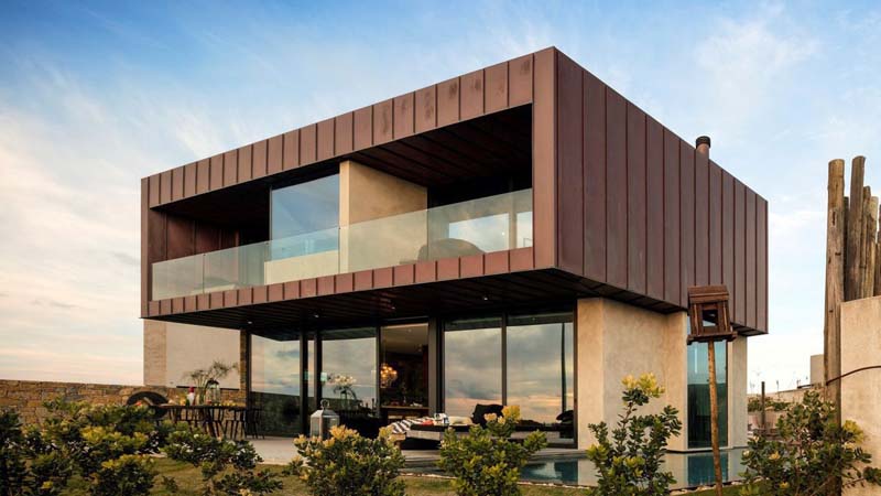 A two-storey building with huge windows and sliding doors to the terrace. It has two balconies and a flat roof. The first floor is covered with a metal coating. 