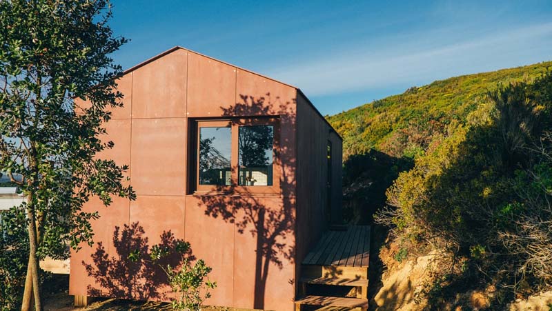 Small house covered in rustic brown metal panels on the side of the hill. 