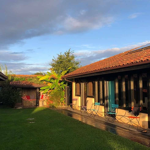 A one-storey brick and wooden house with a green garden in the front.