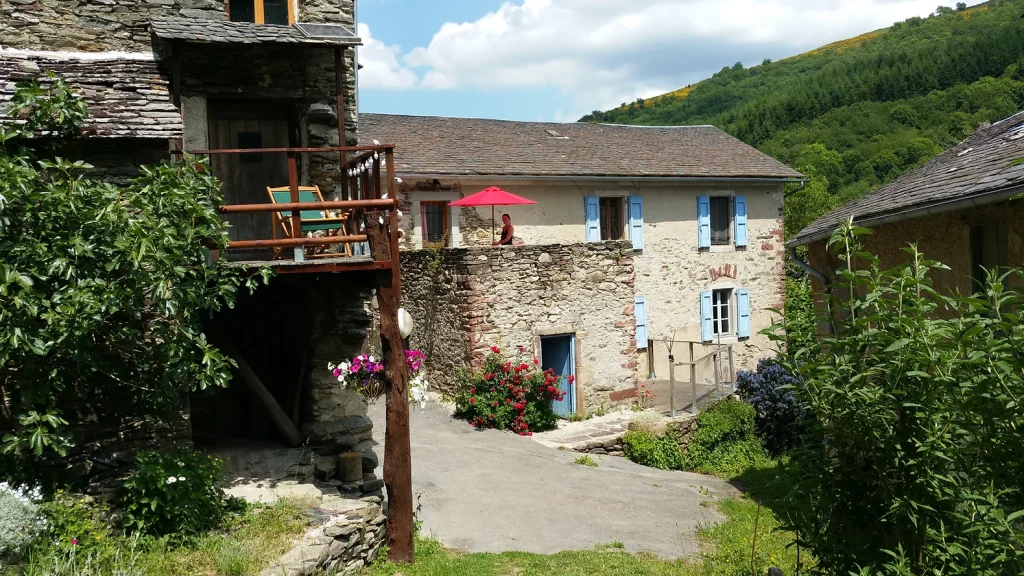 An old stone house with light blue windows and a wooden terrace.