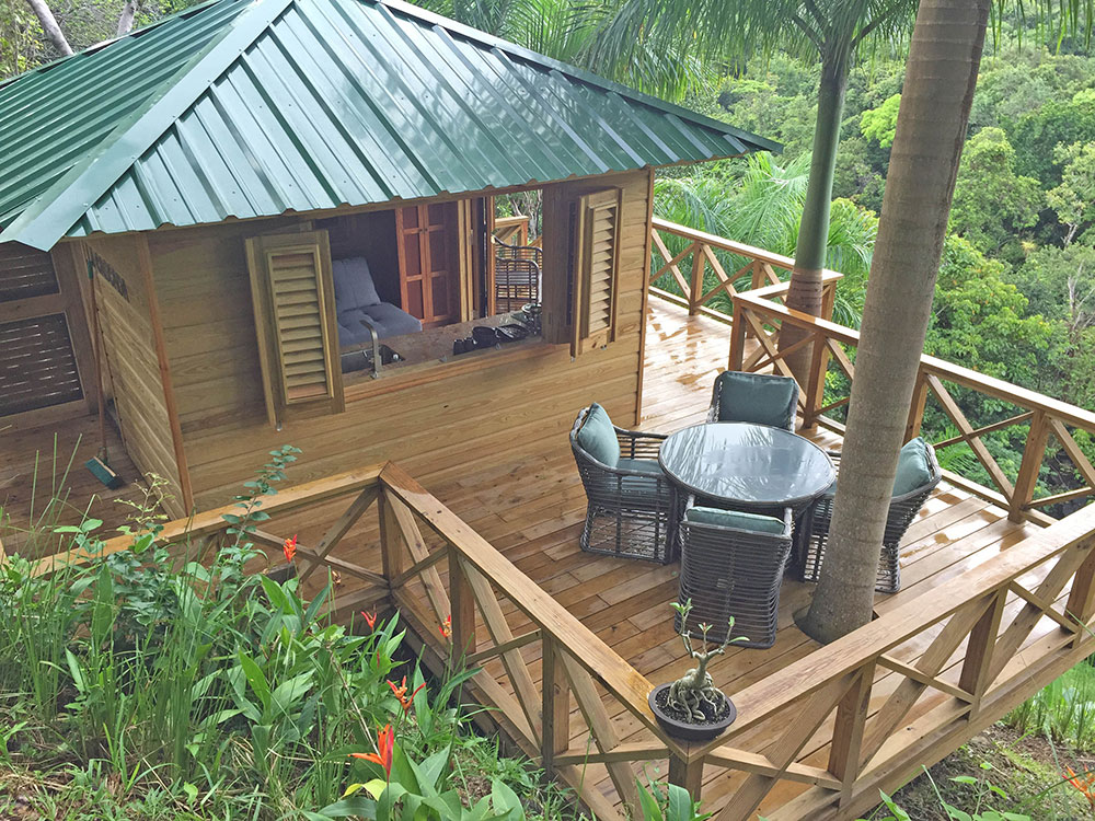 Wooden treehouse with green metal roof and a small terrace with table and chairs. 