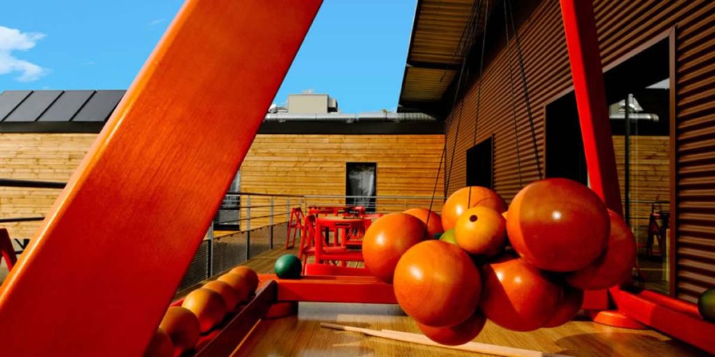 A wooden building with red terrace and furniture and lots of apples hanging in the foreground.