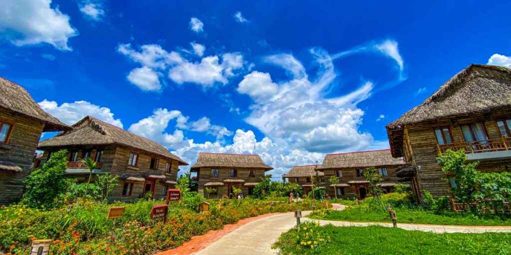 Small wooden buildings with green grass in front of them and bright blue sky with clouds above