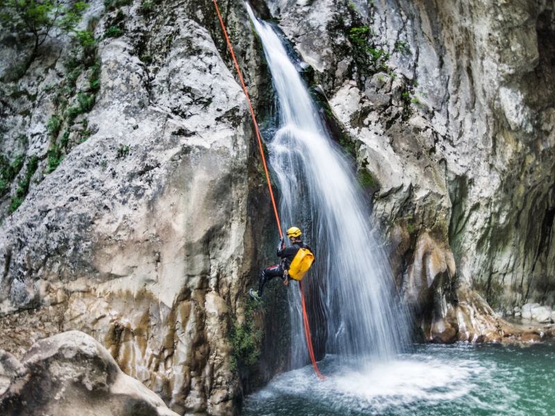 A man is climbing in a waterfall with a red rope.