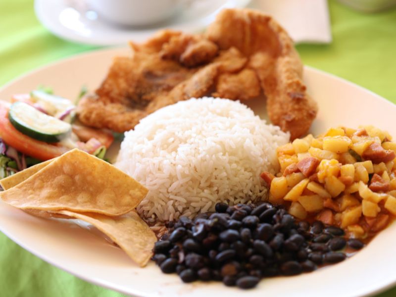 Rice, black beans, chips, and other deep fried food is on a plate.