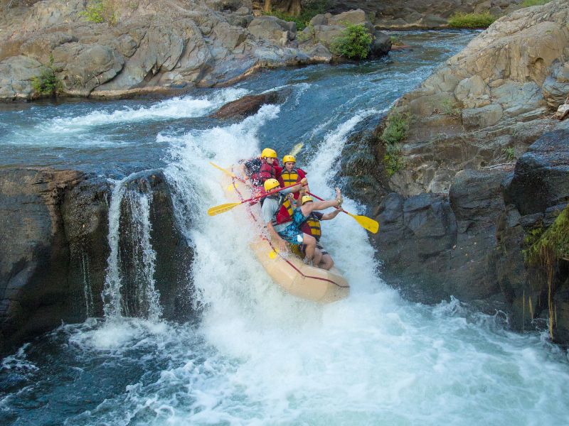 A couple of people in a raft jumping over a small rapid.