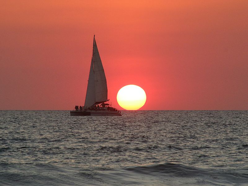 A sail boat with a sunset where the full round of the sun is visible