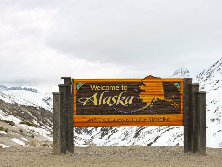 Wooden sign in front of snowy mountains saying welcome to Alaska
