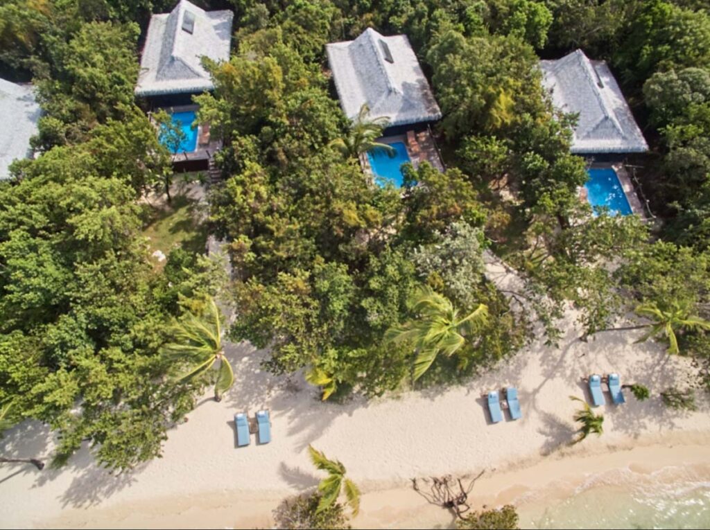 Sandy beach with green forest and small buildings with swimming pool