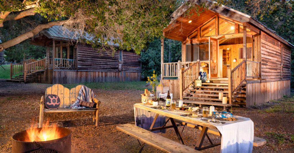 Small wooden cottages in the forest with a fire pit, swing and the table set for dinner.