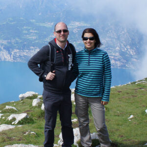 A woman and a man are standing on a mountain. Behind them there is a lake.