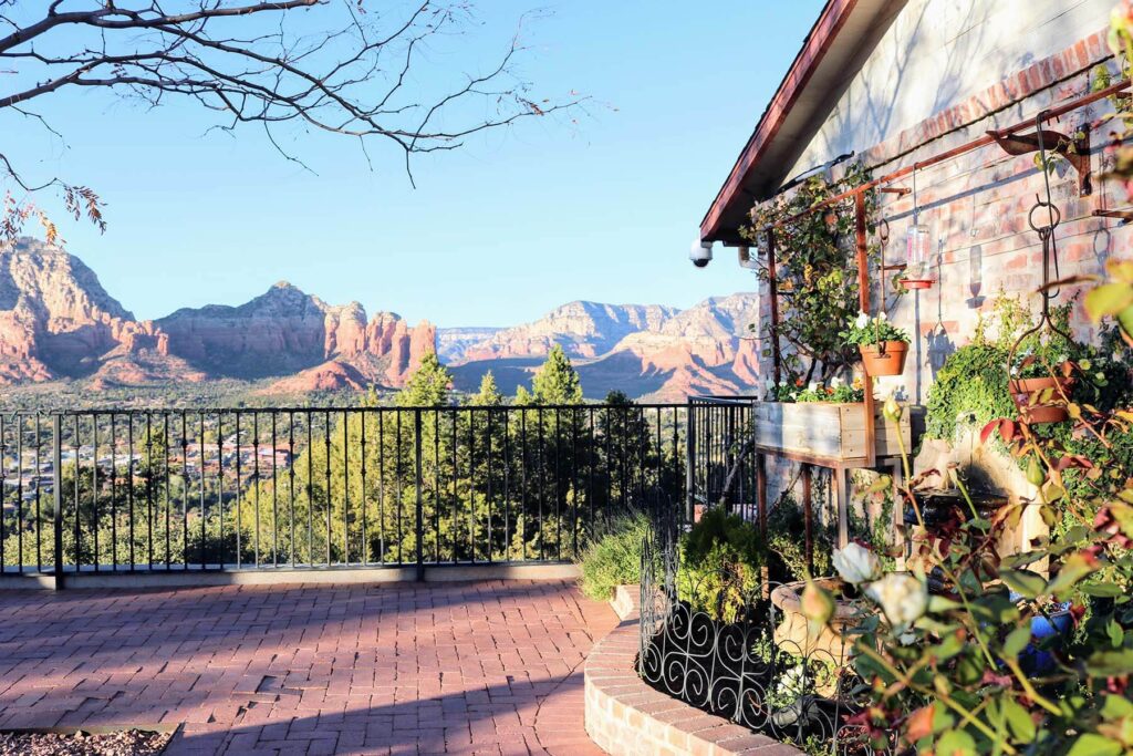 A stone covered house with a red brick garden overlooking large mountains. 