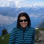 A woman sitting on a mountain. Behind her is a lake.