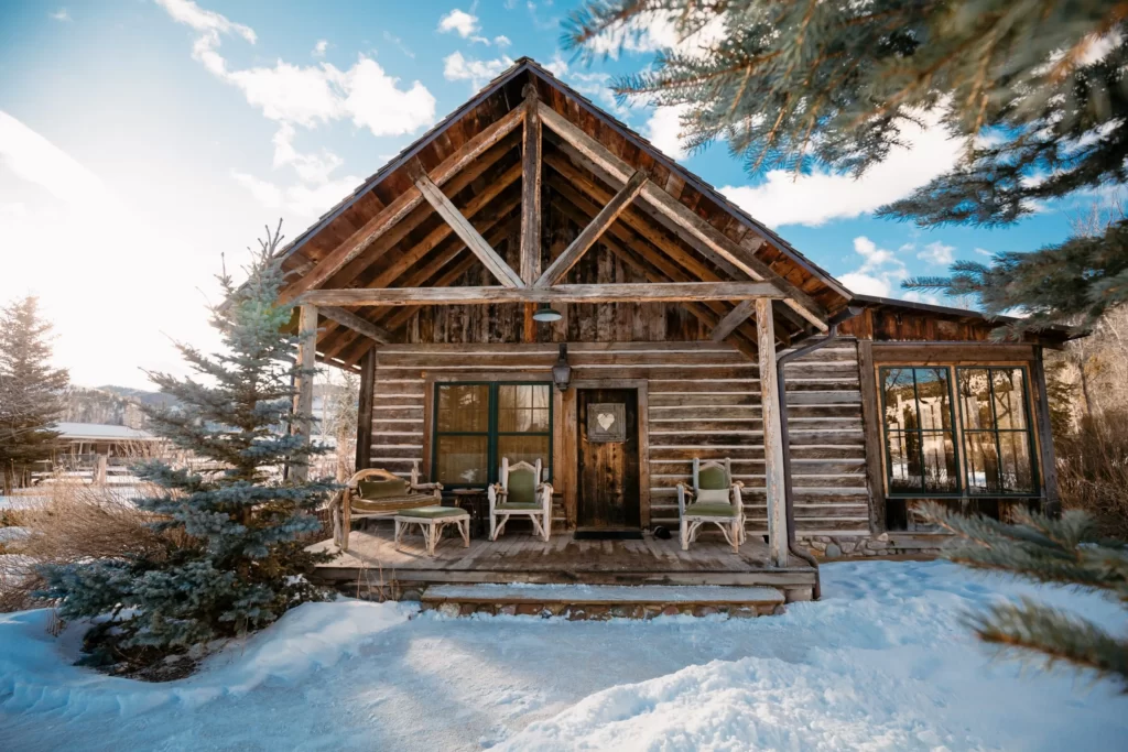 A wooden cottage surrounded by pine trees and snow