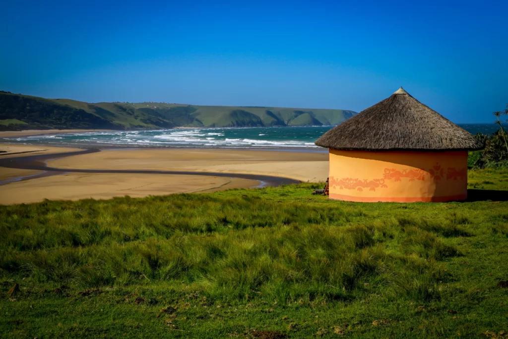 An orange hut with straw bale roof on a small grassy hill overlooking the ocean