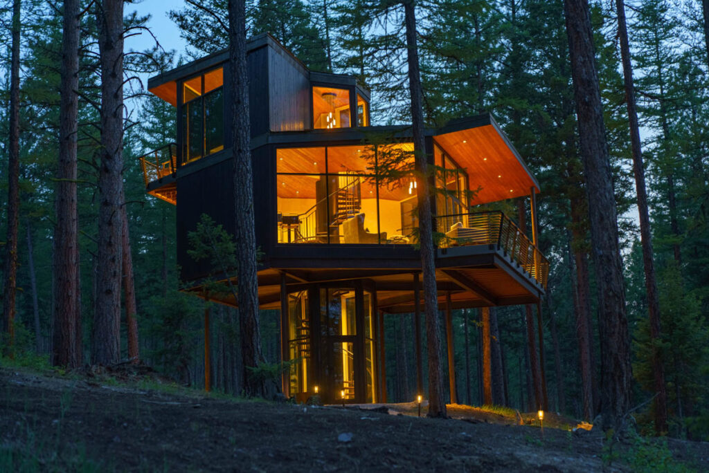 A treehouse in the woods at night with lights on inside.