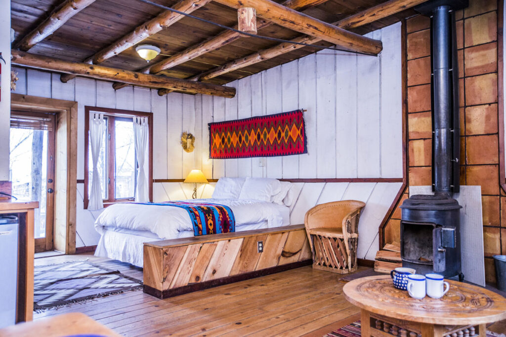 Room with double bed, white wooden walls, and wooden ceiling.