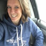 A women with a blue hoodie is sitting in a car and smiling