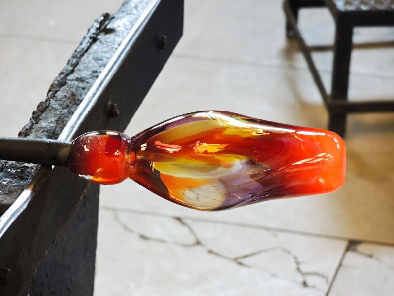 Red yellow purple hot melted glass is at the end of a large stick