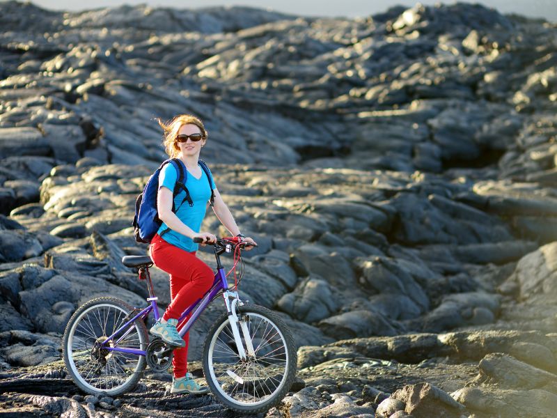 A woman in a blue T-shirt and red jeans riding a bike on black cold lava. 