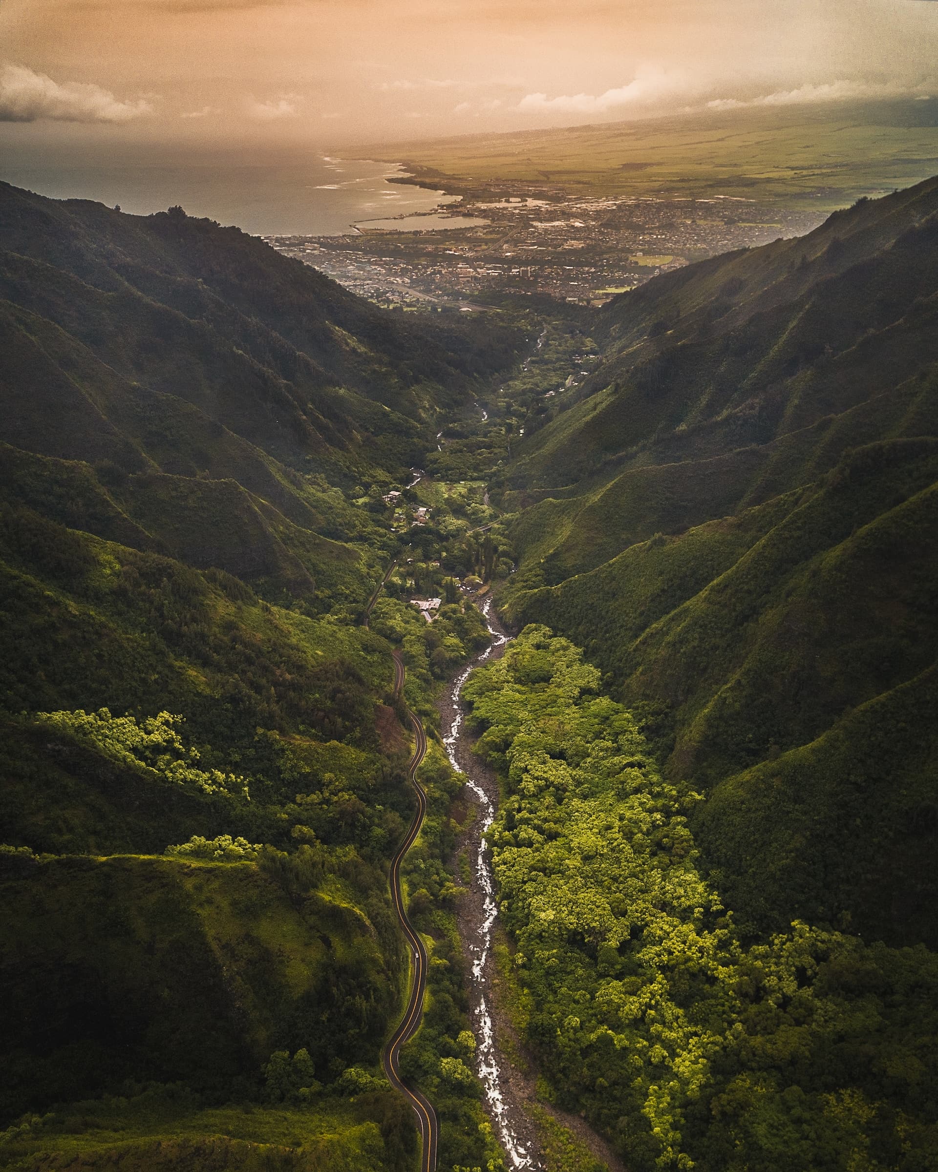 Aerial view of a stream in the valley with mountains and jungles flowing towards a city and the ocean