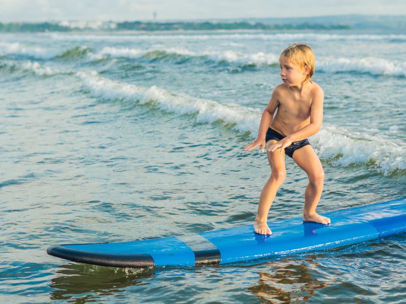 A kid is standing on a blue surf around small waves. 